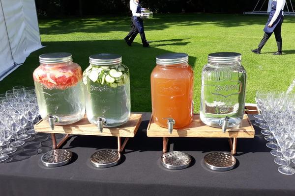 Photo of four glass water decanters on a table with various soft drinks inside