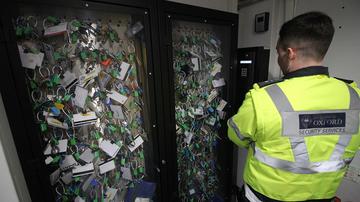 Photo of a man wearing Security Services hi-vis jacket looking at a cabinet full of many different keys and access cards