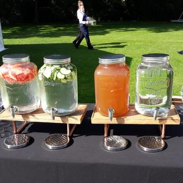 Photo of four glass water decanters on a table with various soft drinks inside